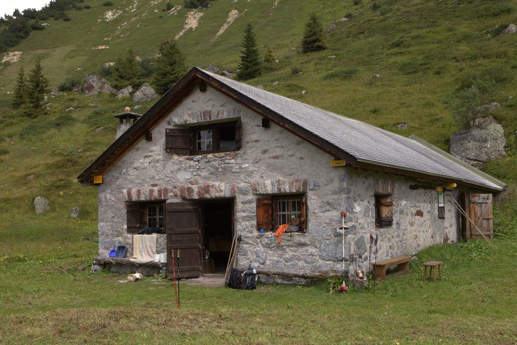 A restored stone cottage with wooden shutters on a green alpine hillside