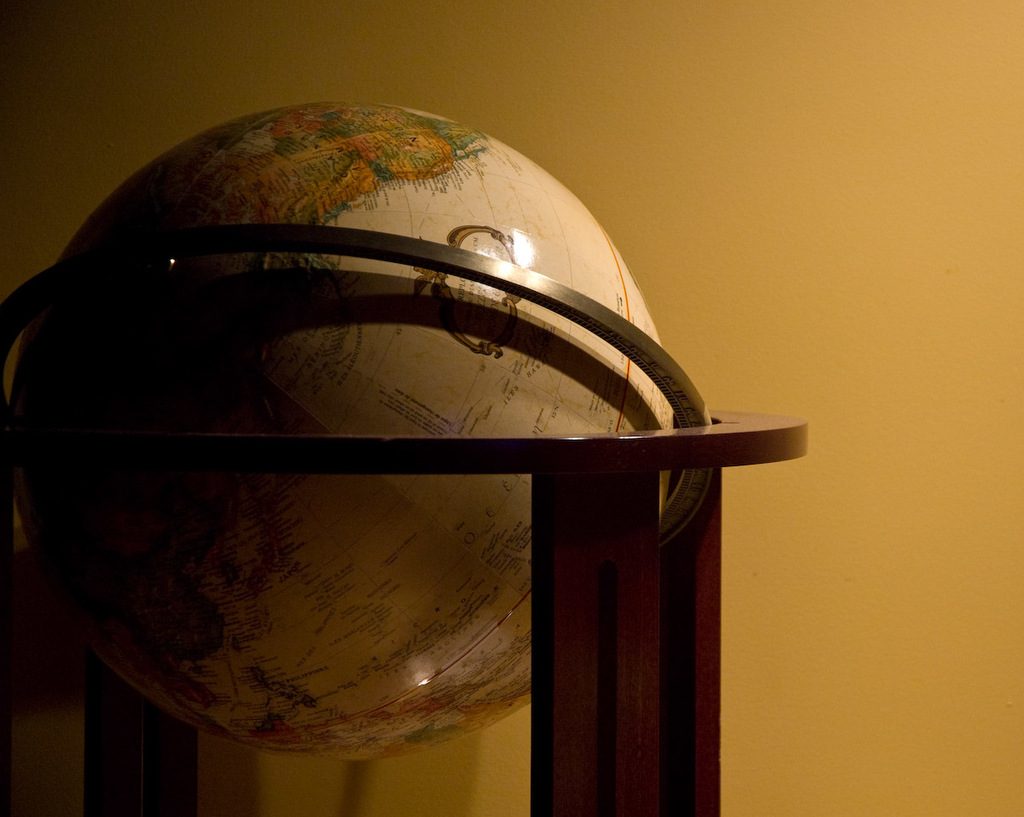A large vintage world globe in a dark wooden stand glowing in warm light