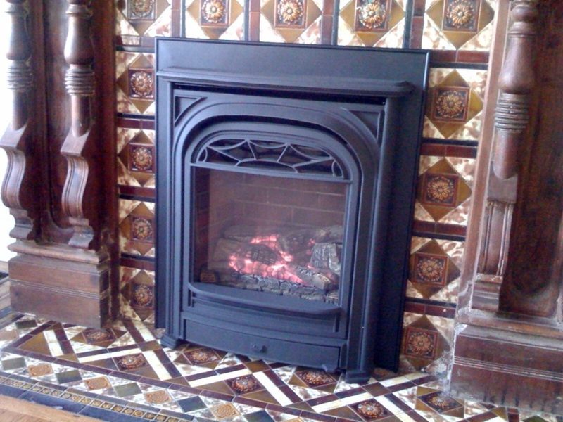 A black enclosed fireplace insert set into a tiled surround with carved wooden columns
