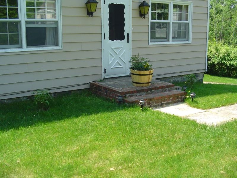 A cream sided house with brick front steps, a potted plant and a green lawn