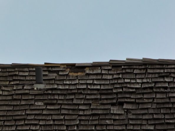 Weathered cedar shingles along a roof ridge under a pale sky